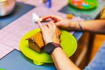 Close up view of  woman assembling gingerbread house on green plate during calm Christmas crafting moment. Sweden.