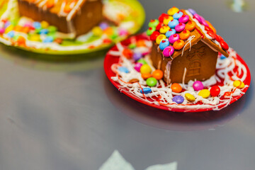 Close up view of small gingerbread house covered with colorful candies and icing on red plate for Christmas celebration. Sweden.