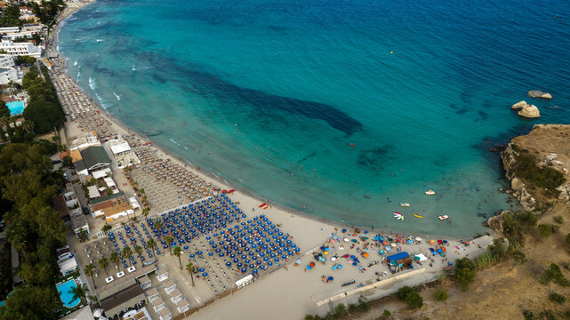 Aerial view of Fontane Bianche beach, located in the province of Syracuse, Sicily, Italy. There are many beach resorts with their umbrellas overlooking a blue, crystal-clear sea. It is a sandy beach.