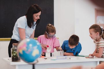 Elementary School Science Classroom: Enthusiastic Teacher Explains Chemistry to Diverse Group of Children, Little Boy Mixes Chemicals in Beakers. Children Learn with Interest