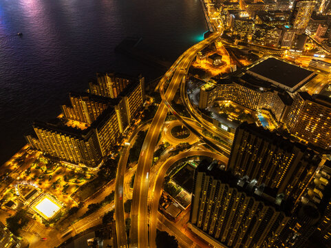 Aerial view of gleaming highways and buildings radiating a golden glow against the dark sea near the Hong Kong Convention and Exhibition Centre, Hong Kong, Hong Kong Island, Hong Kong.
