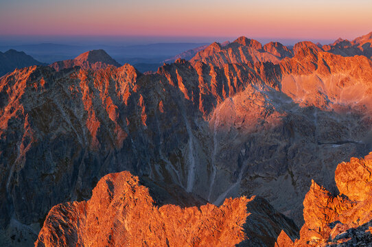 Aerial view of jagged peaks ablaze with the fiery hues of dawn, casting long shadows across the rugged landscape, Vysoke Tatry, Presov Region, Slovakia.