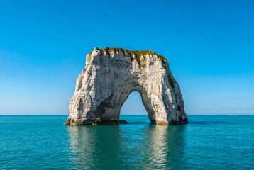 Tretat white chalk cliff archway in bright blue sea under clear sky