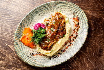 Rich, slow-braised beef short ribs on a bed of creamy garlic mashed potatoes with herb garnish and...