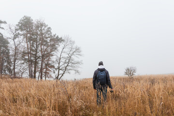 Man in jacket and pants with backpack is walking with camera in winter fog landscape. Hobby background