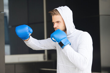 Sportsman in boxing gloves outdoor. Young man boxer. Sport man boxing. Strong athlete man. Sportsman in hoodie. Strong boxer in sportswear. Exercising and punching. Practicing boxing. Uppercut strike