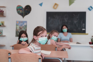Multiracial group of kids wearing face masks working at class, writing and listening explanations of teacher in classroom