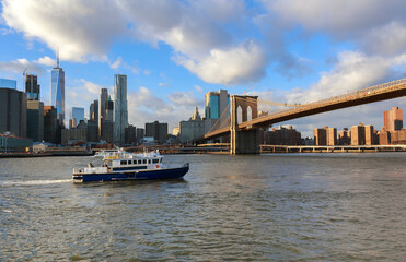Ferry passing under Brooklyn Bridge with skyscrapers in New York City