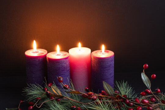 Four advent candles lit on an advent wreath with greens and red berries