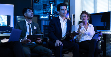 Diverse team of cybersecurity experts, business professionals, and IT specialists intently monitors data on a screen in control room. Teamwork, technology, and corporate security strategy