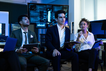 Diverse team of cybersecurity experts, business professionals, and IT specialists intently monitors data on a screen in control room. Teamwork, technology, and corporate security strategy