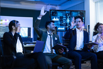 Diverse group of smiling data analysts and IT professionals collaborating in a meeting. Colleague raises his hand enthusiastically to share an innovative solution during a successful strategy session
