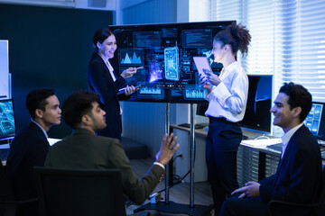 Female executive leads a crucial discussion, presenting complex data and cybersecurity analysis on screen to diverse team of analysts at command center. Global business strategy, financial technology