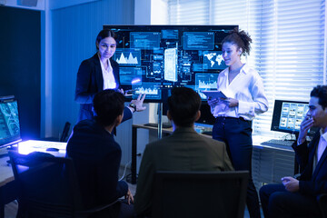 Female executive leads a crucial discussion, presenting complex data and cybersecurity analysis on screen to diverse team of analysts at command center. Global business strategy, financial technology