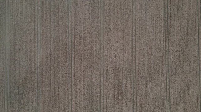 An aerial view of a tilled field, showing parallel furrows from agricultural work. The textured surface suggests dry soil.