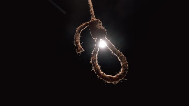 Sinister hangman's noose made of thick jute rope swinging slowly in a dark, scary room with a single spotlight in the background, symbolizing death, despair, and capital punishment