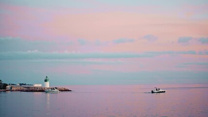 Boats heading toward a small green and white lighthouse near Port Camille Rayon under pastel clouds in Vallauris, France