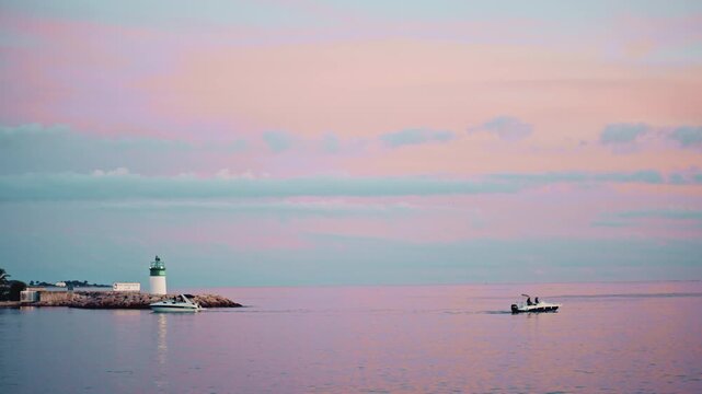Boats heading toward a small green and white lighthouse near Port Camille Rayon under pastel clouds in Vallauris, France