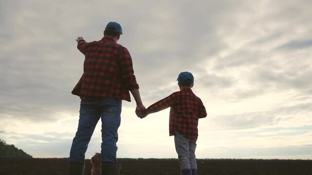 Father and son in a field. Silhouette of farmers and their son plowing a field. Family holding their father sons hand. A dad and his son in lifestyle a meadow.
