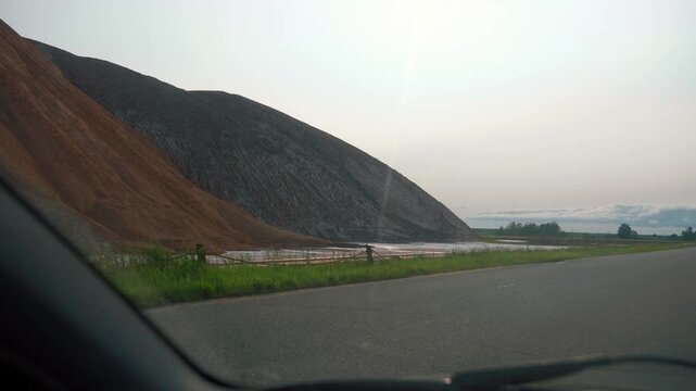 Massive slag heap of industrial mining waste, showing a stark contrast between reddish-brown and gray materials, with visible erosion patterns creating a surreal, man-made landscape