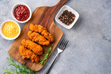 Fried chicken breast strips on grey table background. Delicious chicken crisps