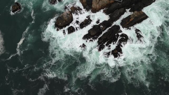Dramatic top down aerial view of ocean waves breaking over large rock.