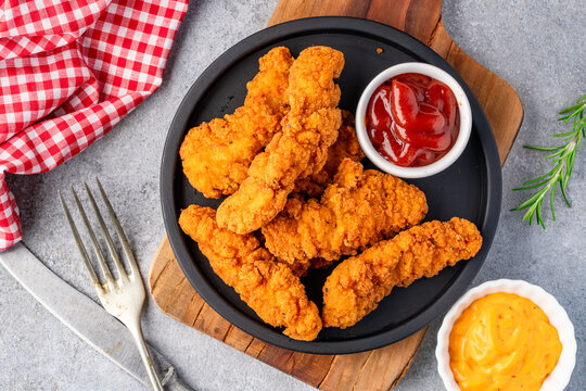 Fried chicken breast strips on grey table background. Delicious chicken crisps