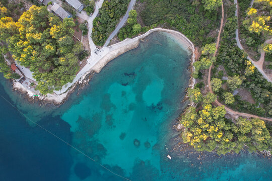 Aerial view of the cove's teal waters meet the rugged coastline, bordered by vibrant green trees casting shadows on the sandy beach, Stari Grad, Split-Dalmatia County, Croatia.