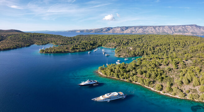 Aerial view of yachts resting in the turquoise waters near the lush green, tree-covered coastline of Stari Grad, Split-Dalmatia County, Croatia.