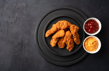 Fried chicken breast strips on black table background. Delicious chicken crisps	
