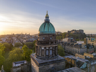 Aerial view of the golden cross atop St. George's West Church dome contrasts against the distant Edinburgh Castle, West End, Scotland, United Kingdom.