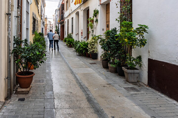 Obraz premium Tourists strolling through a charming alleyway in a white Spanish village on a sunny day.