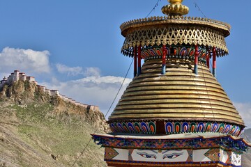 Ornate tip of the Kumbum Stupa at Pelkor Chöde Monastery in Gyantse, Tibet, with the historic Gyantse Dzong fortress rising on the mountain, showcasing Tibetan Buddhist architecture and heritage