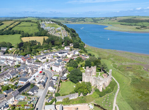 Aerial view of the ancient Laugharne Castle standing proudly against the shimmering Taf Estuary, with homes nestled closely together, Laugharne, Carmarthen, Wales.