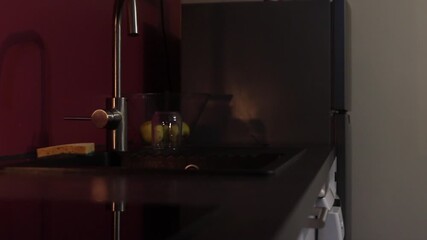 Soft glow from a fashionable mesh lamp fades in a modern kitchen, as the camera slowly pans to the right to unveil a chic faucet, sink, and refrigerator, promoting an eco friendly message