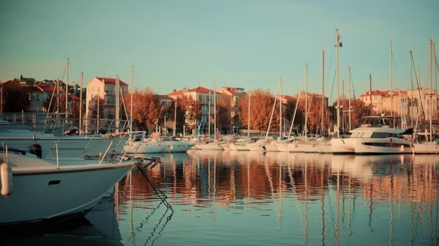 Peaceful marina scene with yachts and sailboats anchored in still water during golden hour