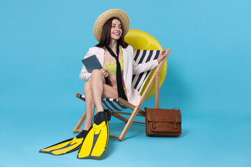 Businesswoman with laptop and flippers in deck chair on light blue background © New Africa