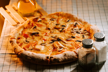 Pizza topped with cheese, chicken, and mushrooms served on a checked cloth table