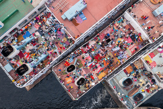 Aerial view of ferries packed with people, their vibrant clothing a stark contrast to the dark water below, creating a bustling scene, Dhaka, Dhaka Division, Bangladesh.