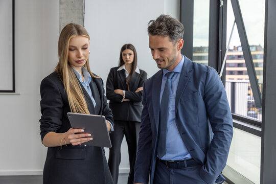 A jealous businesswoman observes a conversation between two colleagues.