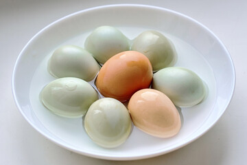 Eggs arranged in flowerlike circle inside white bowl, natural shell colors, simple design, organic farm produce, and healthy nutrition for cooking. Selective focus
