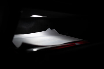 Dramatic macro shot of an open car glovebox at night. The interior light illuminates papers,...