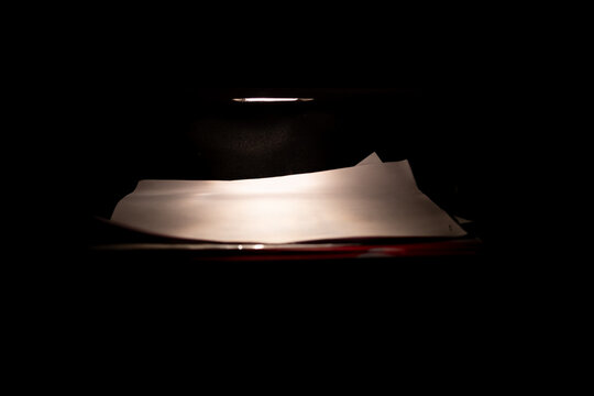 Dramatic macro shot of an open car glovebox at night. The interior light illuminates papers, creating a moody, mysterious, and confidential atmosphere.