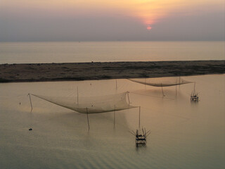 Aerial view of serene, shimmering waters reflecting a soft, pastel sky, with traditional fishing nets casting delicate shadows on the tranquil bay, Hoai Nhon, Binh Dinh, Vietnam.