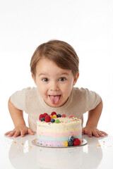 Young Caucasian child leans forward with tongue out, excited by colorful cake topped with fruit and candy. A joyful moment of celebration, ideal for birthday, party, or playful food content.