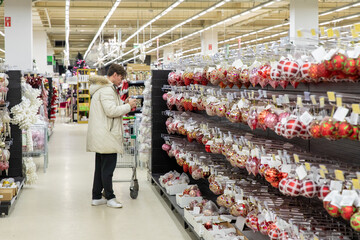 Side view young man in white jacket standing with shopping cart in mall or store and choosing toys...