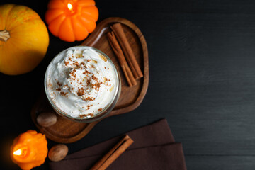 Delicious pumpkin latte with whipped cream and autumn decor on black table, flat lay. Space for text