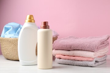 Basket with laundry and bottles of detergent on white wooden table against pink background