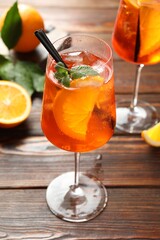 Glasses of refreshing spritzer cocktail and oranges on wooden table, closeup