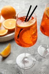 Glasses of refreshing spritzer cocktail and oranges on grey textured table, closeup